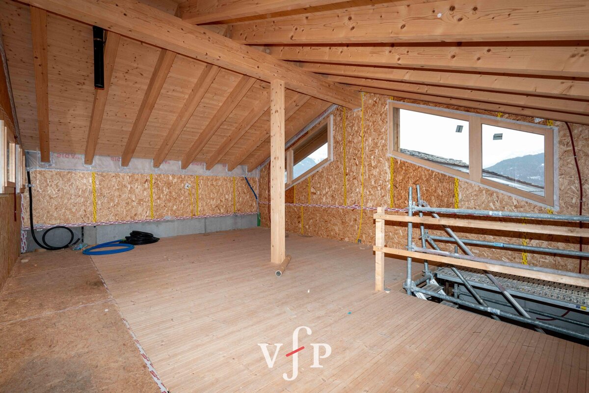 An attic under construction with exposed wooden ceiling beams, OSB walls, floorboards, and safety scaffolding.