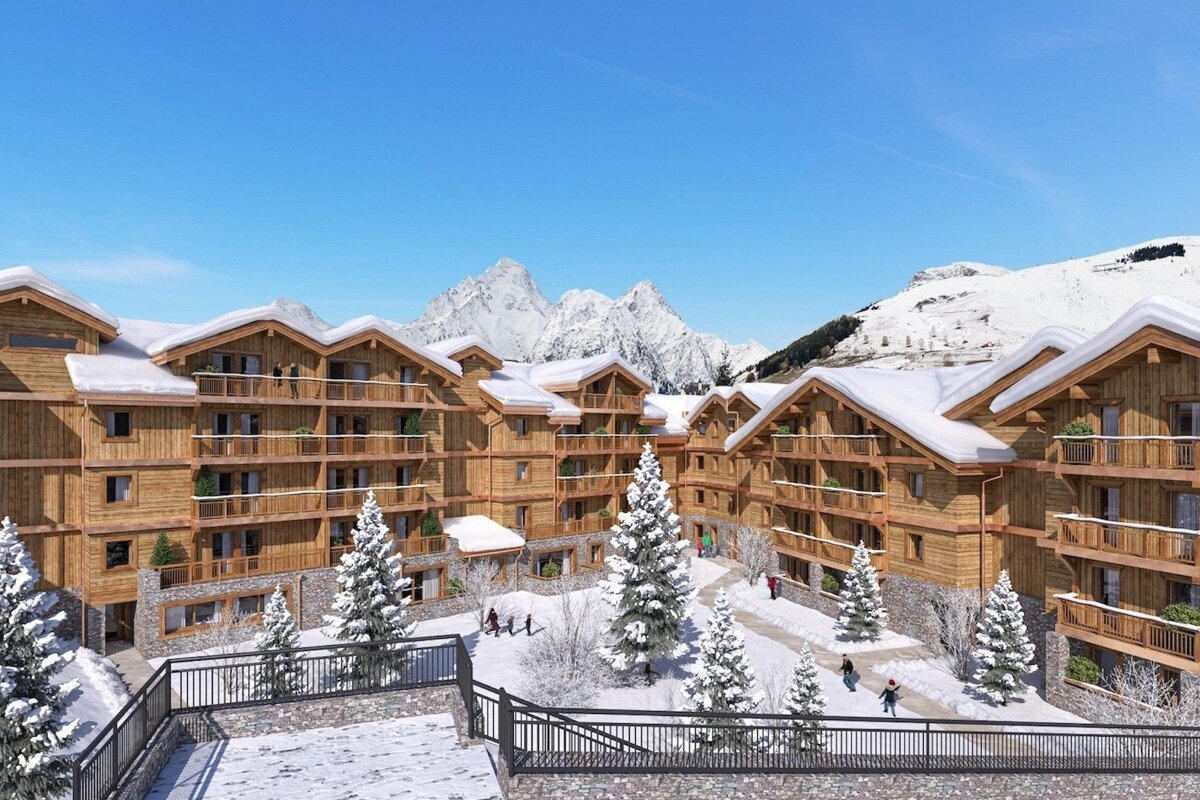 Cozy wooden chalets covered in snow at an alpine resort, with majestic mountains in the background under a clear blue sky.