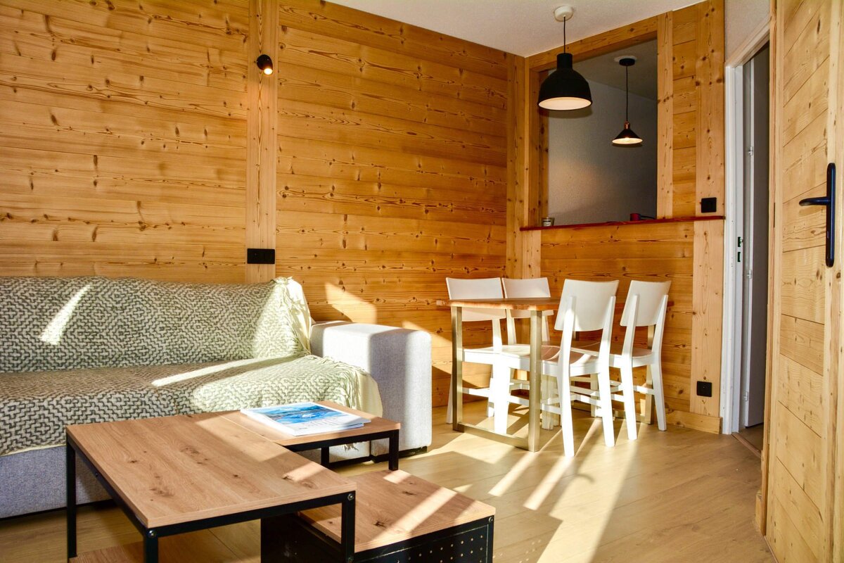 A cozy, modern living room with a gray sofa, coffee tables, and a TV. It features large windows offering snowy mountain views and a deer head wall decor.
