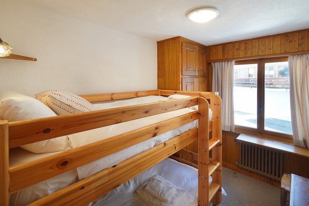 Cozy cabin bedroom featuring a pine bunk bed with white bedding, a wooden wardrobe, and a window.