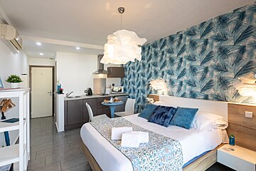 A bedroom with a bed and a kitchen in the background