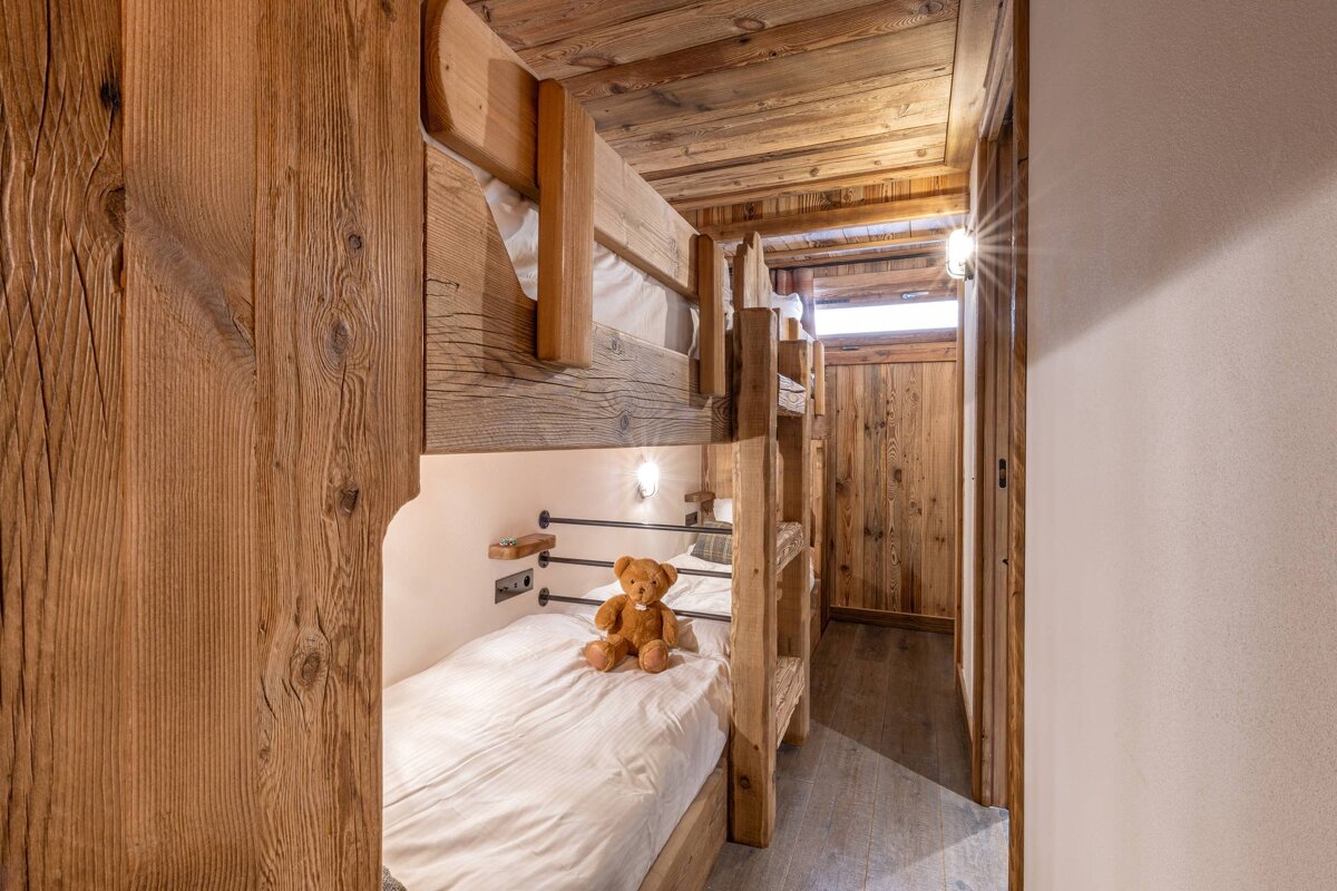 A cozy cabin-style bedroom featuring rustic wooden bunk beds, with a teddy bear sitting on the bottom bunk.