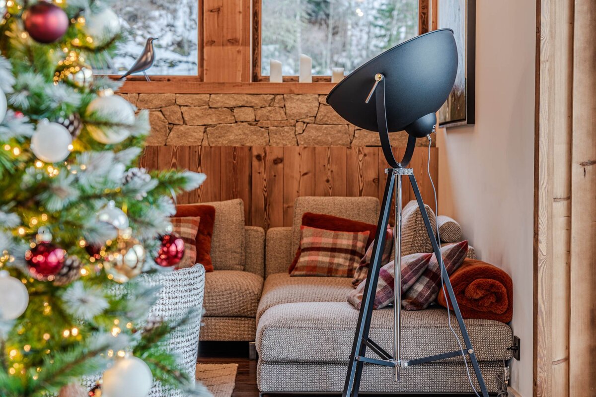 Cozy living room featuring a decorated Christmas tree in the foreground, a grey sectional sofa, and a black tripod floor lamp.