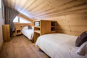A bedroom with two beds and a shelf with towels on it