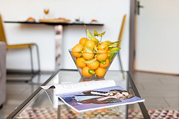 A magazine on a glass table next to a bowl of oranges