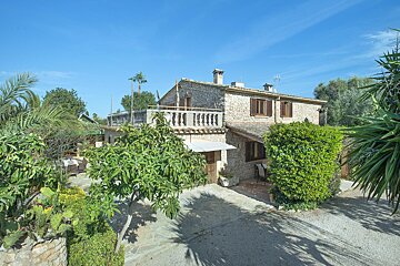 A stone house with a balcony is surrounded by trees and bushes