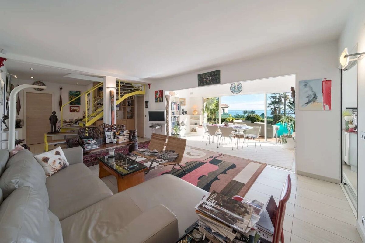 Bright, eclectic living room with a yellow spiral staircase, modern furnishings, and a terrace offering an ocean view.