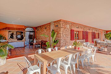 A large wooden table with white chairs in front of a stone wall