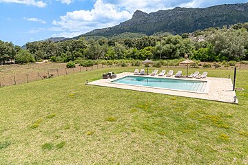 A large swimming pool surrounded by chairs and umbrellas with mountains in the background