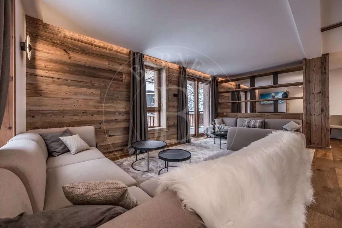 Cozy living room with rustic wood walls, modern sofas, and large windows creating a warm chalet ambiance.
