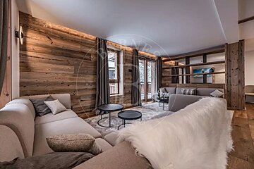 Cozy living room with rustic wood walls, modern sofas, and large windows creating a warm chalet ambiance.