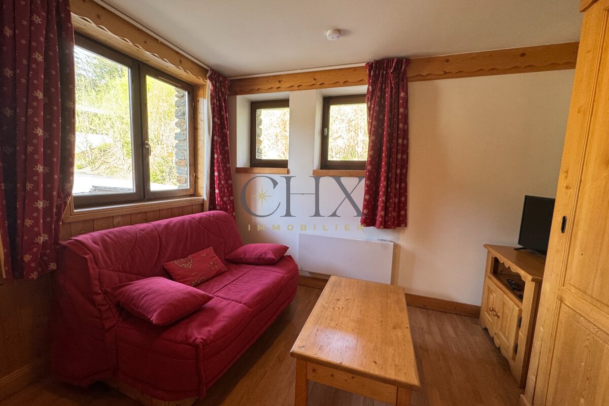 Cozy rustic living room featuring a red sofa, wooden coffee table, matching furniture, red curtains, and windows.