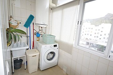 A bright laundry area with a washing machine, utility sink, hamper, and water heater next to a large window.