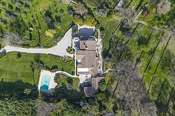 Aerial view of a luxury villa with a swimming pool, surrounded by green lawns, trees, and terraced gardens.