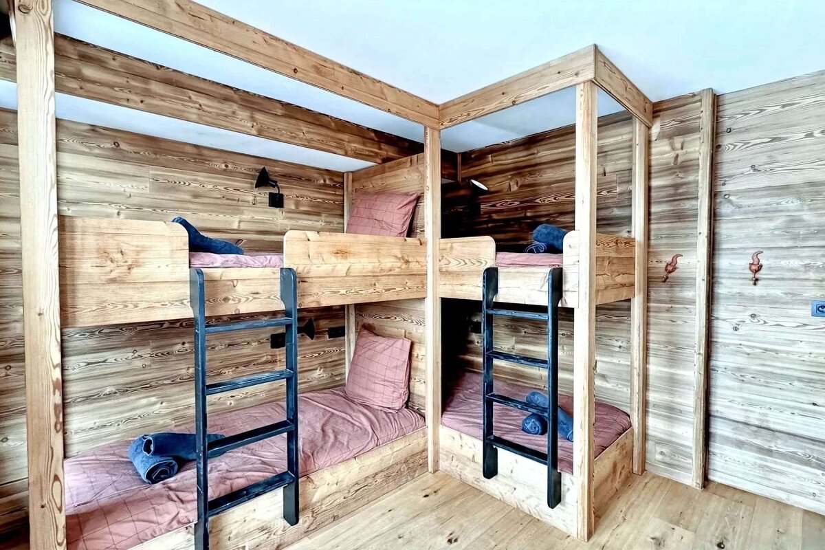 A cozy, rustic wooden room with four bunk beds, each with pink bedding, blue towels, and reading lamps.