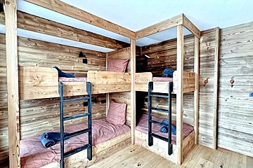 A cozy, rustic wooden room with four bunk beds, each with pink bedding, blue towels, and reading lamps.