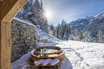 A wooden hot tub in the snow with mountains in the background