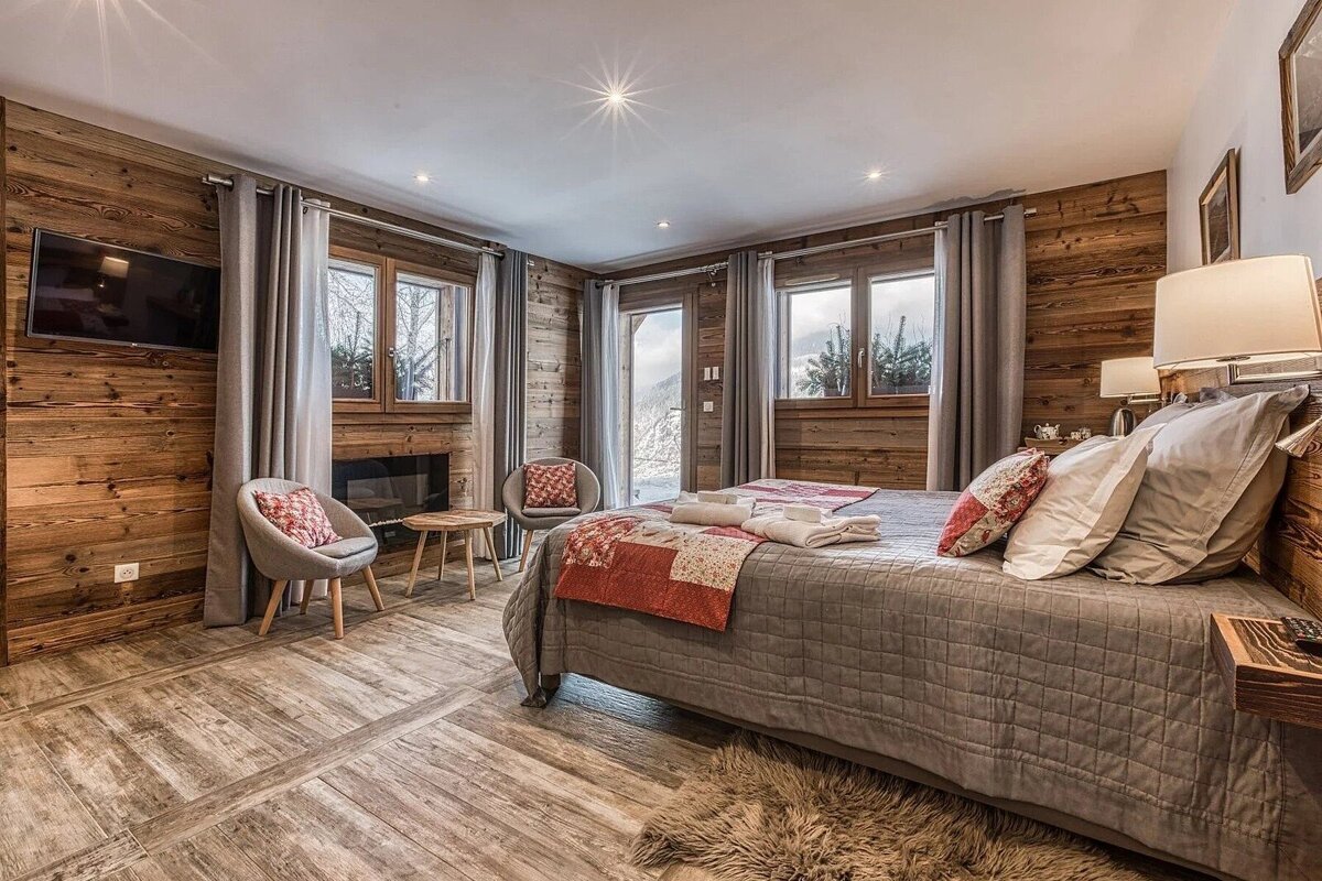 A luxurious chalet bedroom with wood-paneled walls, a large bed, and scenic views of a snowy mountain landscape.