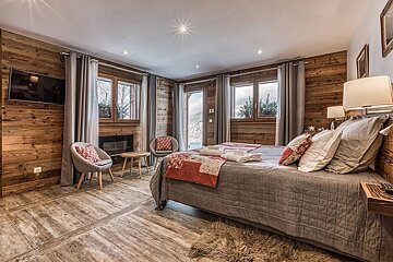 A luxurious chalet bedroom with wood-paneled walls, a large bed, and scenic views of a snowy mountain landscape.