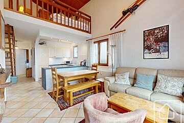 Cozy alpine cabin interior with a living room, dining area, kitchen, and a loft bedroom above.