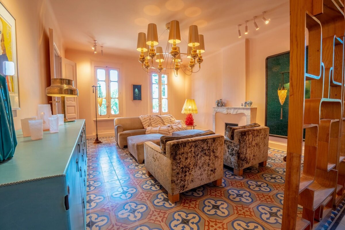 Warm living room featuring patterned tile floors, cozy armchairs, and a large golden chandelier overhead.