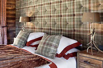 A bed with plaid pillows and antlers on the nightstand