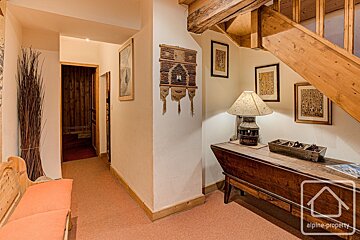 A cozy wooden interior hallway featuring rustic decor, a lamp, a long wooden chest, wall art, and stairs leading up.