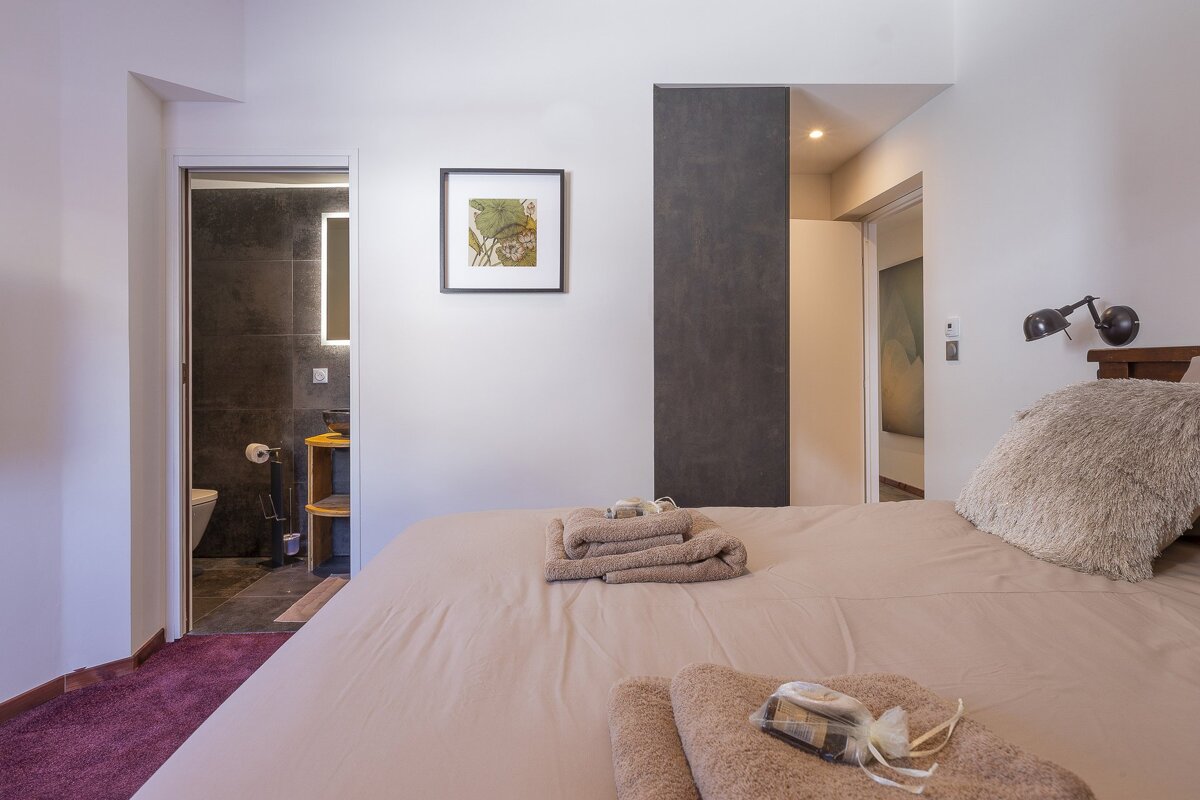 Minimalist bedroom with folded towels on the bed and an open doorway leading to a dark-tiled bathroom.