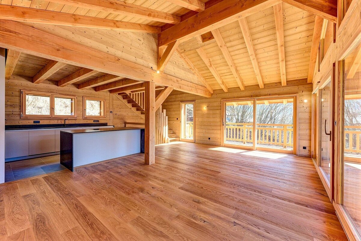 Spacious wooden chalet interior with vaulted ceilings, exposed beams, hardwood floors, a kitchen island, and sliding glass doors.