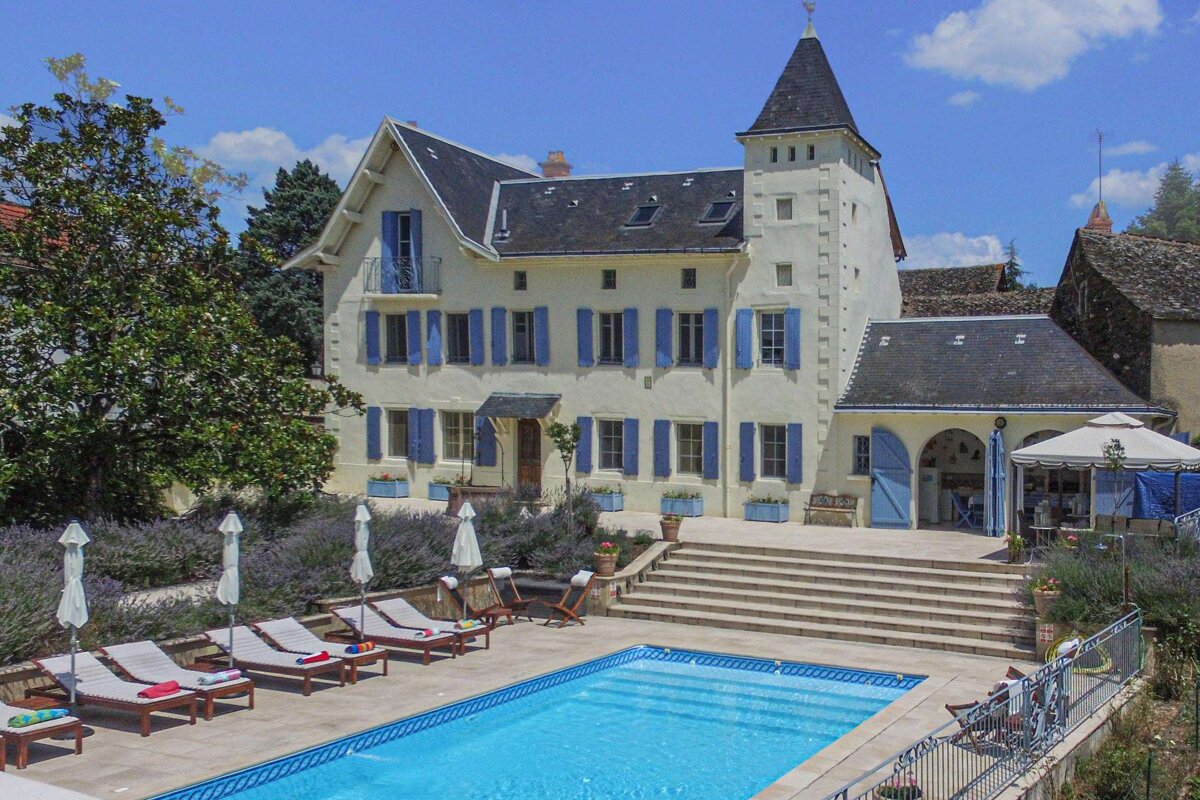 A large white building with blue shutters sits next to a large swimming pool
