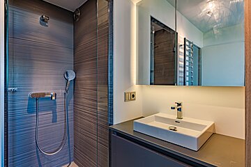 Modern bathroom with a glass-enclosed shower, textured walls, and a vanity with a white rectangular sink, chrome faucet, and an illuminated mirror.