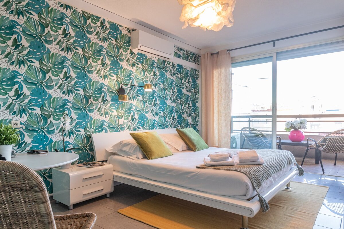 A bedroom with a large bed and a tropical wallpaper on the wall
