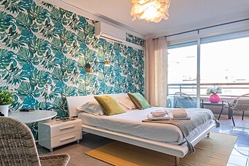 A bedroom with a large bed and a tropical wallpaper on the wall