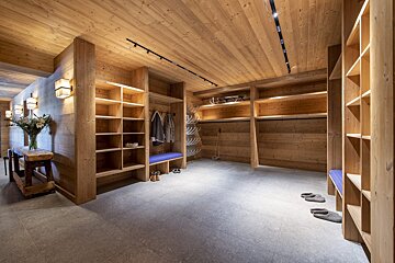 A walk in closet with wooden shelves and a blue bench
