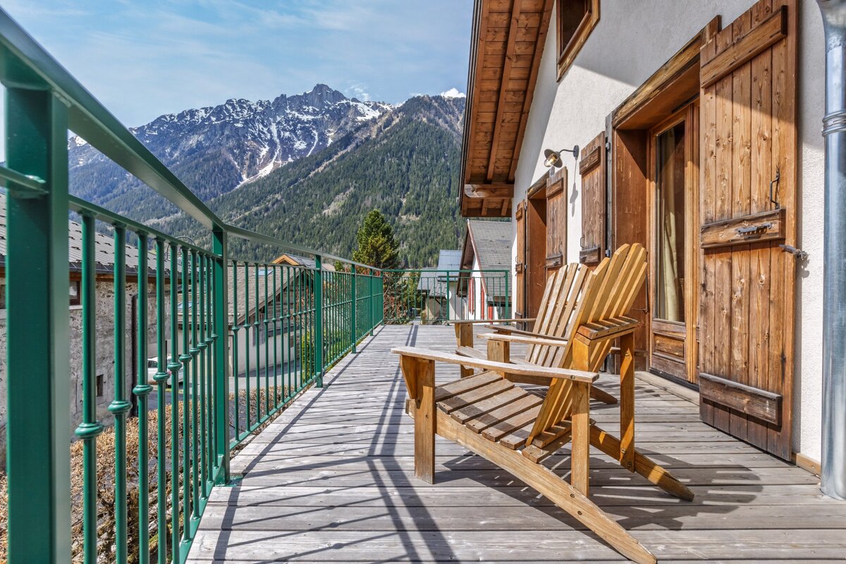 Two wooden chairs on a balcony with mountains in the background