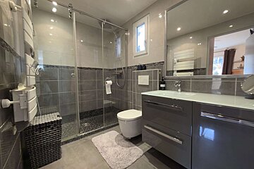 A sleek, modern gray and white bathroom featuring a glass shower, floating toilet, stylish vanity with mirror, and towel warmer.