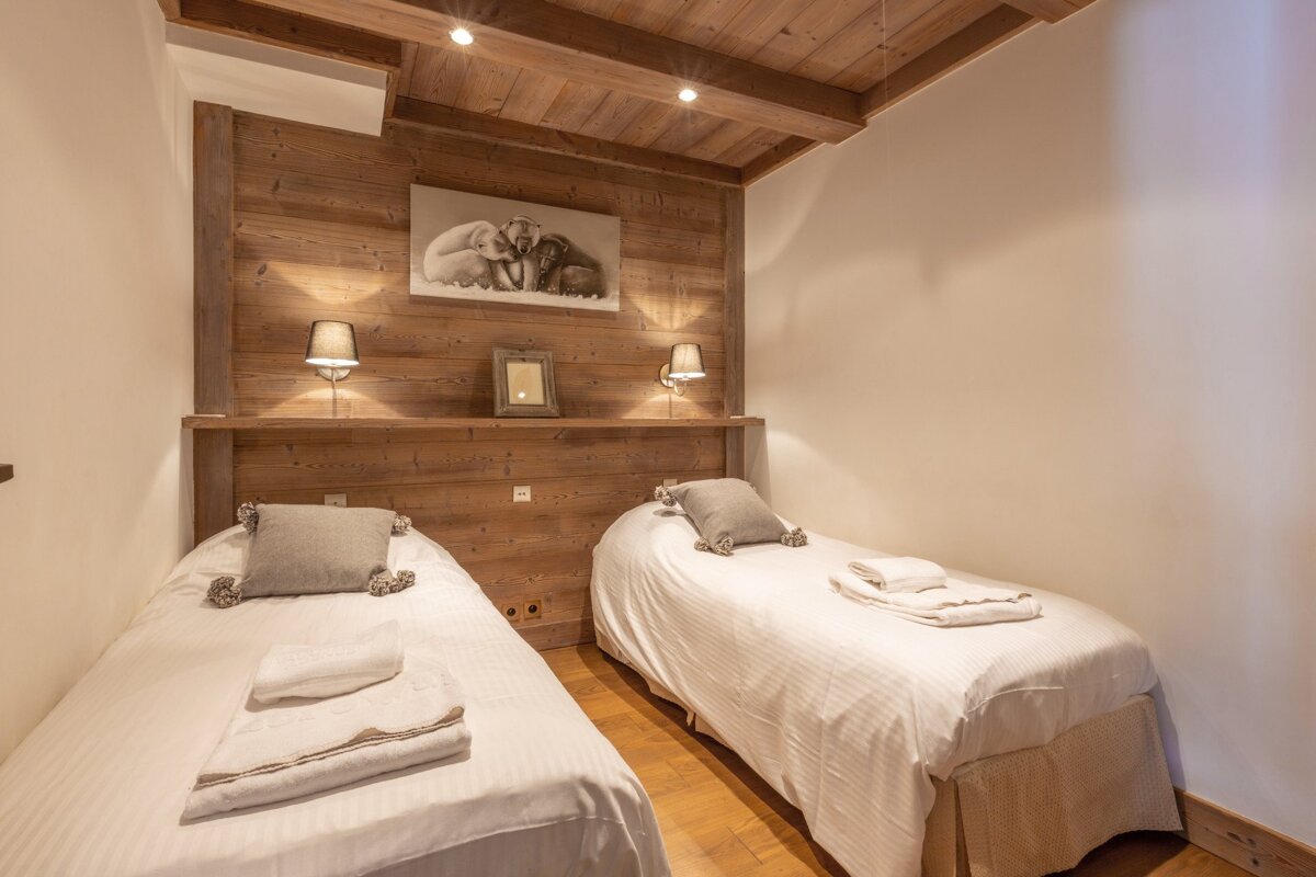 Cozy cabin-style bedroom featuring two twin beds, wood-paneled walls and ceiling, and warm ambient lighting.