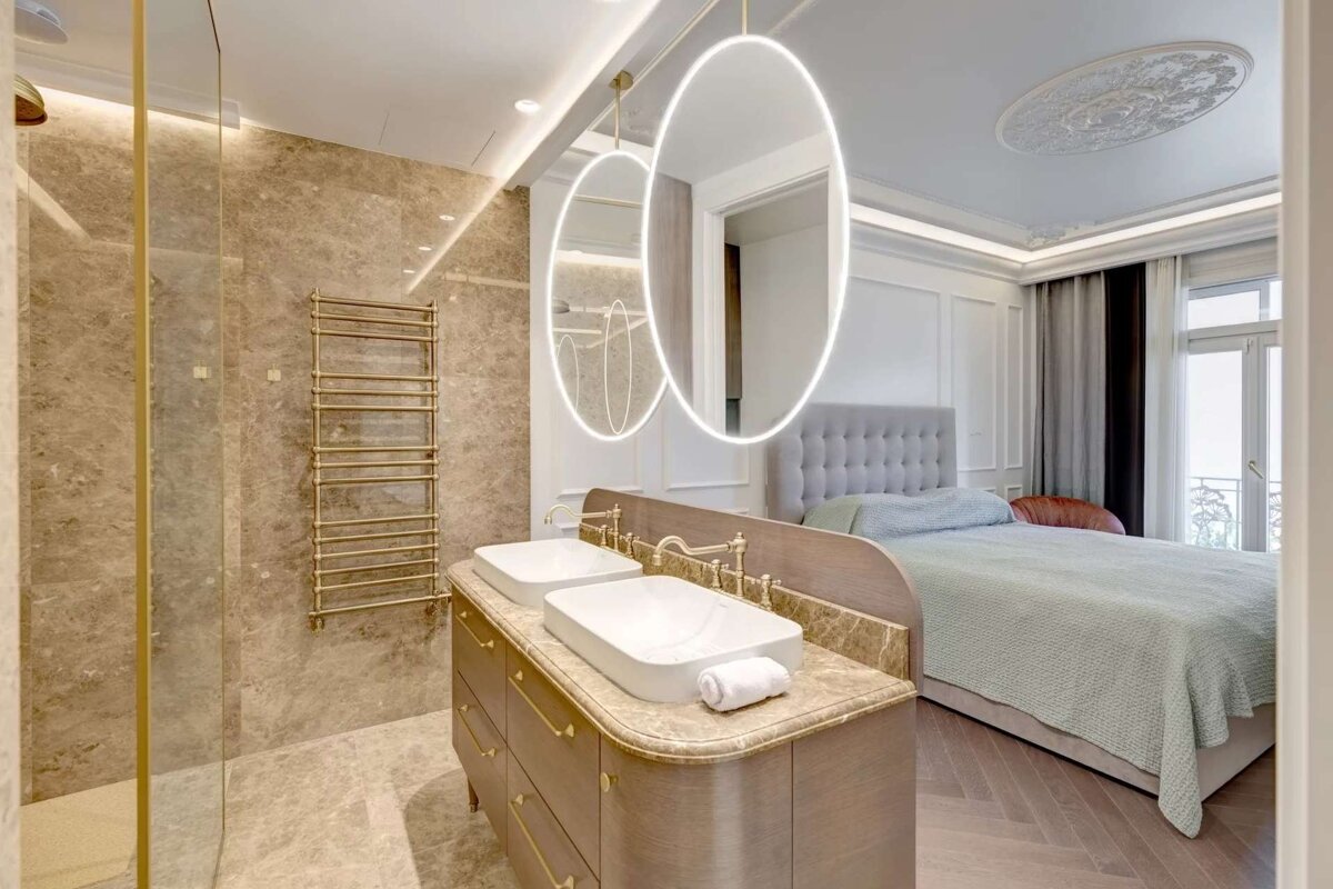 A luxurious open-plan bedroom features an integrated bathroom with a double vanity, shower, and gold accents, blending modern and classic styles.