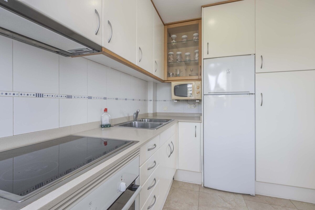 A clean, compact kitchen with white cabinets, white appliances (fridge, oven, microwave), a stovetop, and a double sink.