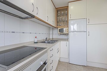 A clean, compact kitchen with white cabinets, white appliances (fridge, oven, microwave), a stovetop, and a double sink.