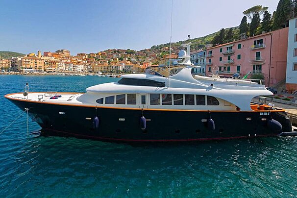 A large yacht is docked in a harbor with buildings in the background
