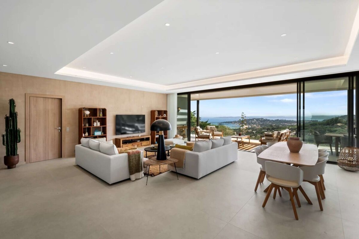 A chic modern living/dining room with expansive sliding doors revealing a breathtaking panoramic sea and mountain vista.