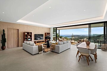 A chic modern living/dining room with expansive sliding doors revealing a breathtaking panoramic sea and mountain vista.