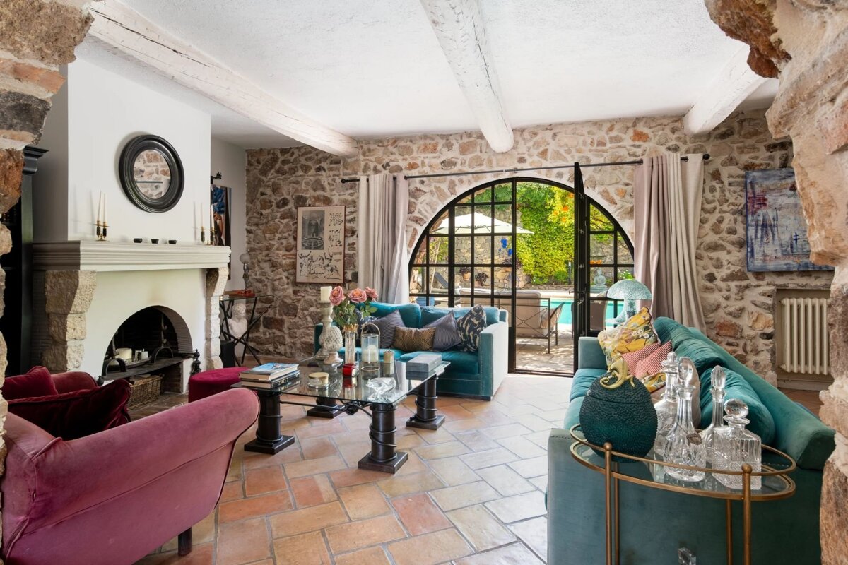 Rustic living room with stone walls, teal and pink sofas, and a large arched glass door leading to a patio.