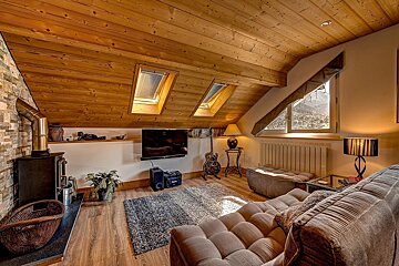 Cozy, rustic attic living room featuring a wood ceiling, skylights, fireplace, TV, and guitar. A comfy sofa faces a mountain view.