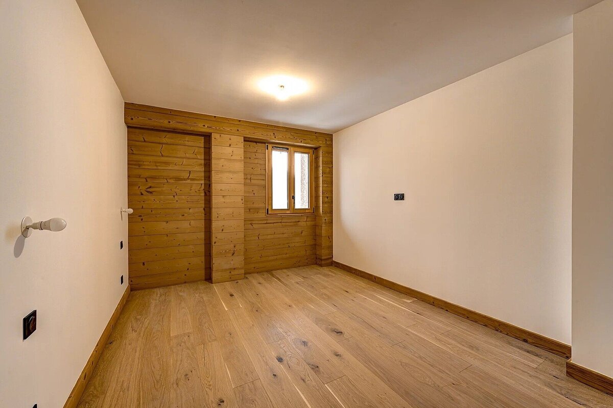 Empty room with light hardwood floors, white walls, and a rustic wooden accent wall with a small window.