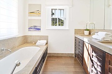 Bright bathroom with built-in tub, double vanity, wood floors, and a window framing green hills. Abstract art, white walls, and clean lines.