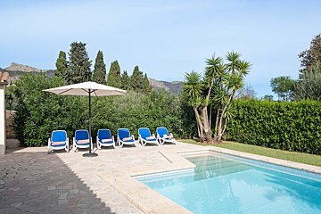 A row of blue chairs under an umbrella next to a swimming pool