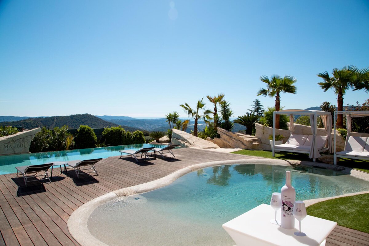 A bottle of wine sits on a table next to a swimming pool
