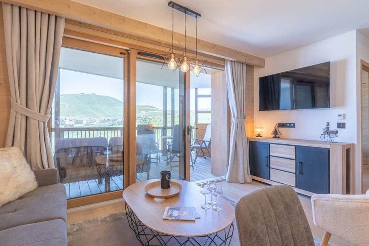 Cozy living room with wood accents, a stylish coffee table, and large glass doors opening onto a scenic mountain-view balcony.
